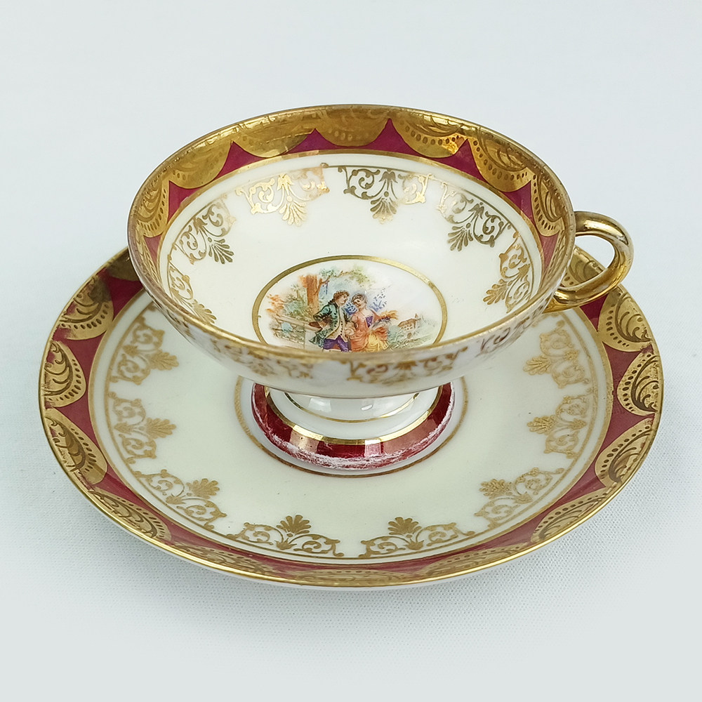 LO 125 – Xícara de cafezinho em porcelana alemã com pé alto decorada com arabescos em ouro e casal romântico